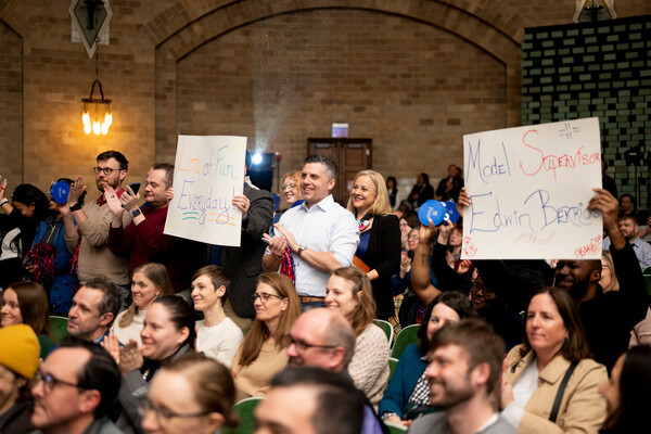 Audience members clapping, cheering, and holding celebratory signs at the 2025 Models of Excellence award ceremony